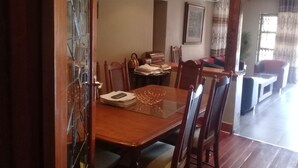 Een eetruimte met een houten tafel en stoelen, een lijst met een afbeelding aan de muur, en een trap naar een ander niveau.