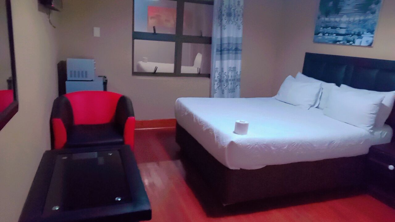 Ein Hotelzimmer mit einem Bett, einem roten und schwarzen Sessel, einem kleinen Tisch und einem Fenster mit Blick nach draußen.