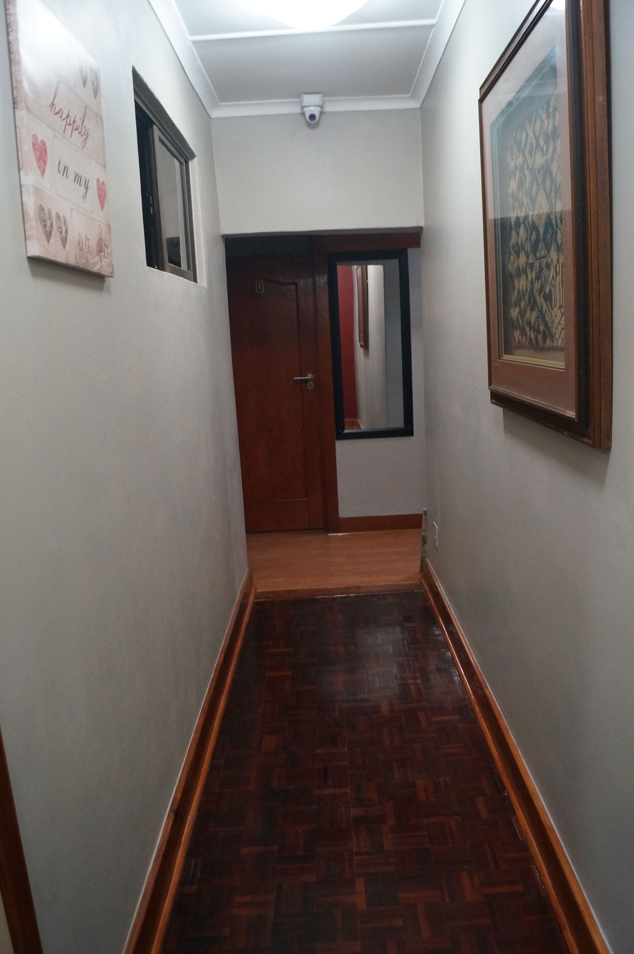 A hallway with a wooden floor, a door at the end, and a framed picture on the right wall.