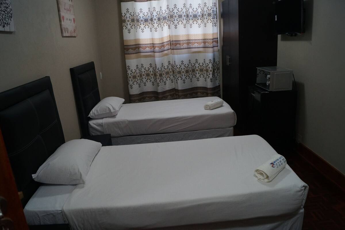 Une petite chambre d’hôtel avec deux lits simples, un téléviseur fixé au mur et un four à micro-ondes posé sur une petite table.