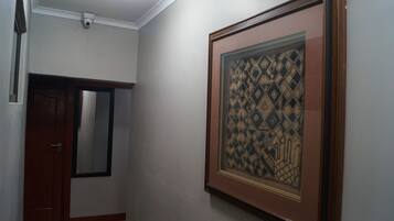 Un pasillo con una obra de arte enmarcada en la pared, una puerta de madera y una cámara de seguridad instalada en el techo.