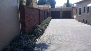 Een geplaveide oprit die leidt naar een garage, begrensd door een bakstenen muur en een haag.
