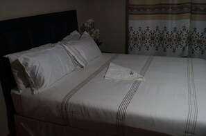 A neatly made bed with white bedding and a single pillow.