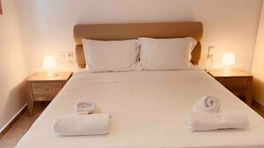 A neatly made bed with two rolled towels, a wooden headboard, and bedside lamps. - Villas Nine Muses - Villa Efterpi 3 bdr villa (Hersonissos)