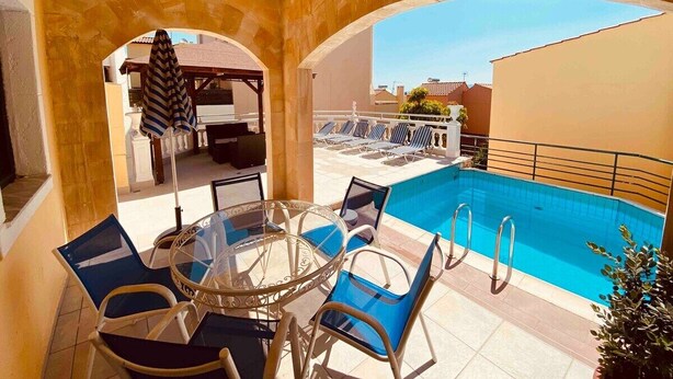 A poolside area with a glass table and chairs, a pool, and a view of the surrounding buildings. - Villas Nine Muses - Villa Efterpi 3 bdr villa (Hersonissos)