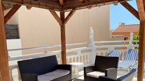 An outdoor patio area with wicker furniture, a white statue, and a view of buildings in the background. - Villas Nine Muses - Villa Efterpi 3 bdr villa (Hersonissos)