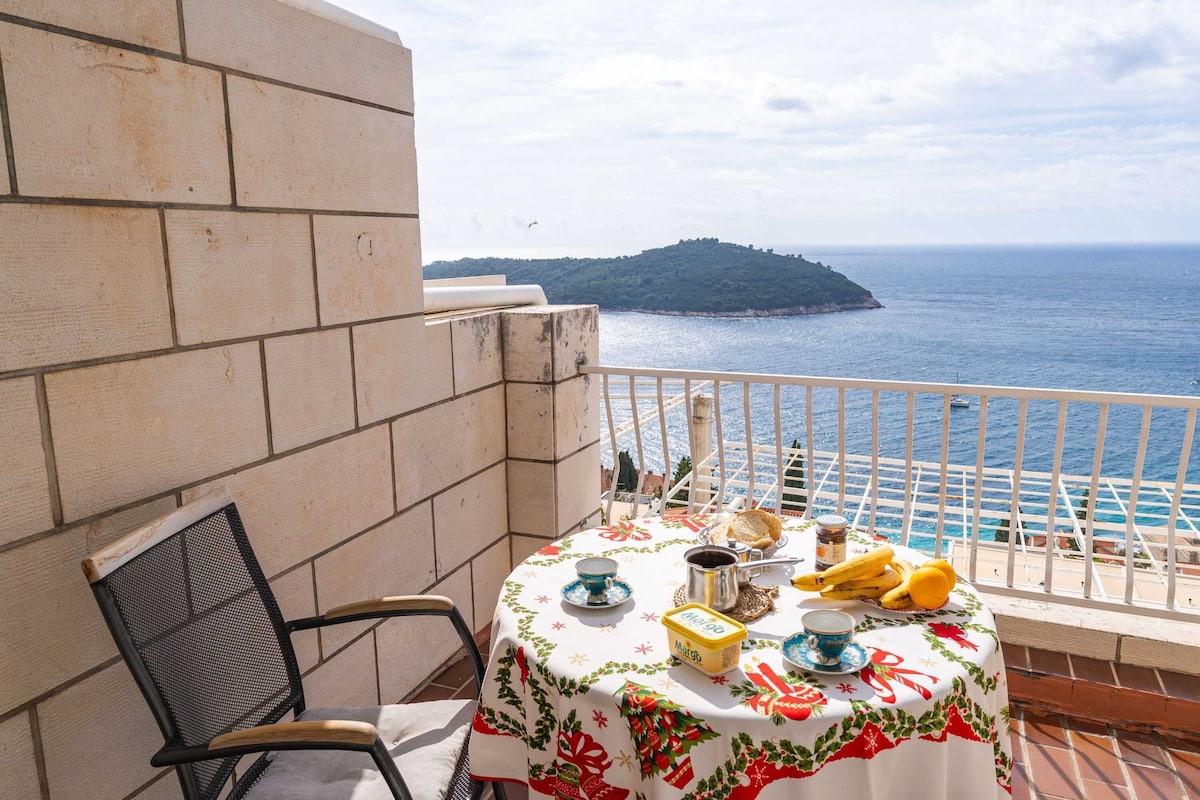 A balcony with a table set for breakfast, overlooking the sea and a distant island.