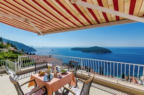 A balcony with a striped awning overlooking a coastal view. - Apartments Cicko (Dubrovnik)