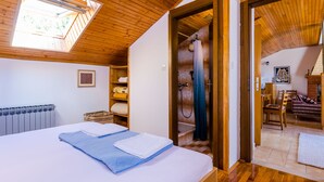 Un dormitorio con tragaluz, una cama con ropa de cama azul y blanca, techo de madera y vista a otra habitación con un sofá y un cuadro.