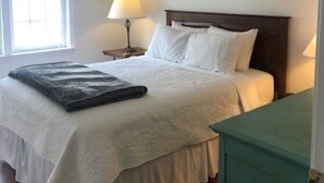 A neatly made bed with white linens, a bedside lamp, and a painting on the wall.