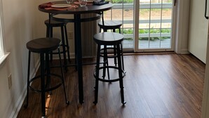 A dining area with a table and four stools, a sliding glass door leading to a balcony, and a white refrigerator.