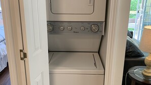 A compact, white washer and dryer unit in a small laundry room with a door leading to a balcony.