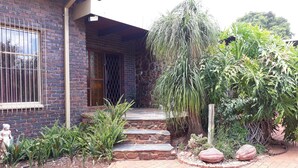 A brick house with a stone staircase leading to a door, surrounded by various plants and a garden. - Die Plasie (Pretoria)