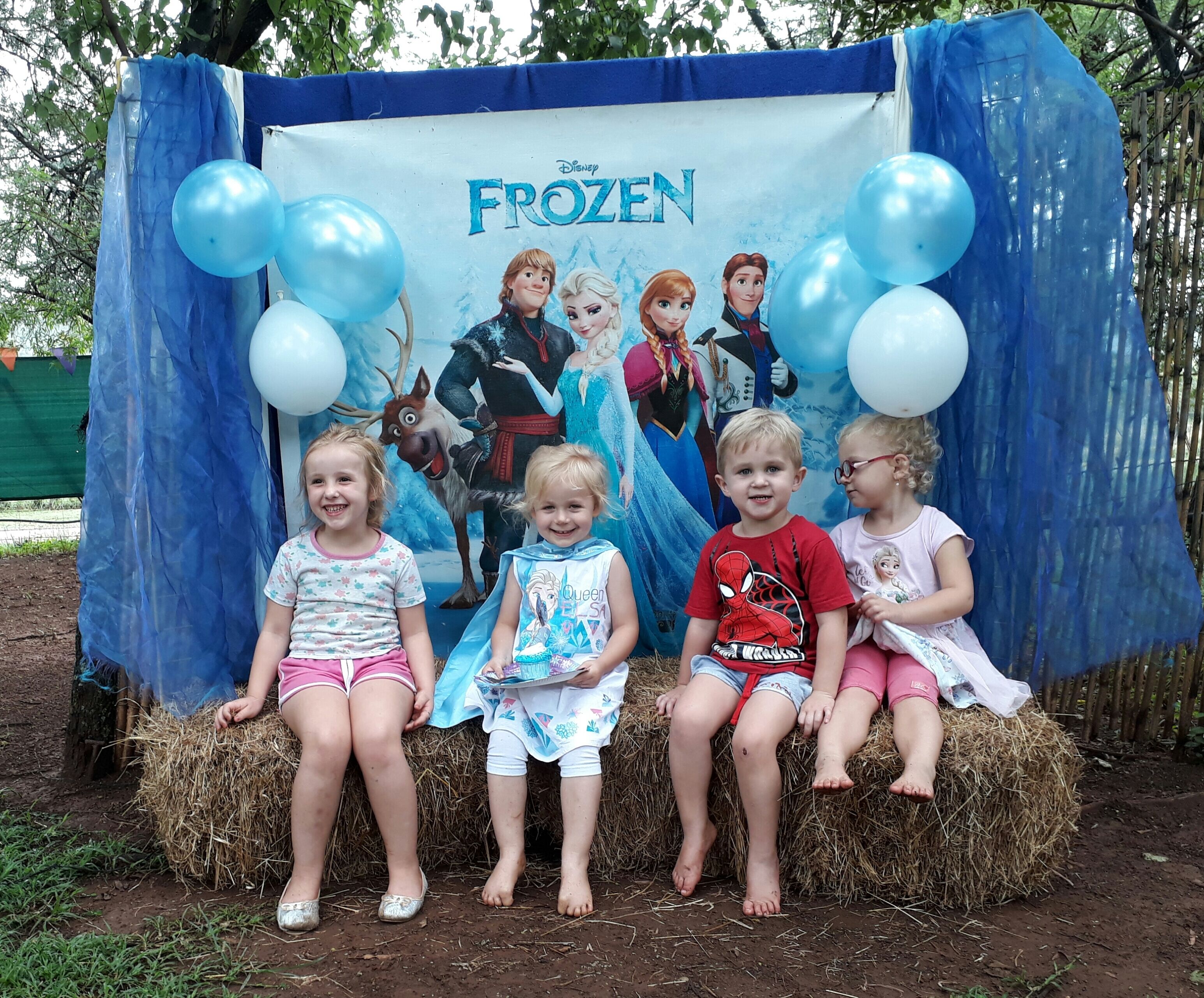 Um grupo de crianças sentadas em fardos de feno em frente a um cenário da Disney Frozen.