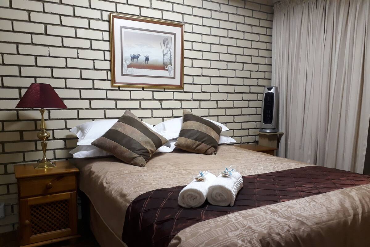 Une chambre d’hôtel avec un mur décoré d’un motif en briques, un tableau encadré, un lit avec des oreillers à rayures, une table de chevet avec une lampe et un téléviseur.