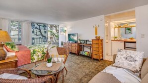 A cozy living room with a sofa, a dining table, and a TV. There's a kitchen area with a counter and cabinets.