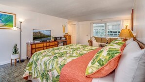 A bedroom with a bed, a desk, a television, and a window.