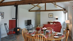 Zona pranzo con tavolo in legno apparecchiato per quattro persone, televisione e divano rosso sullo sfondo.