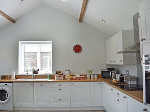 A kitchen with white cabinets, a wooden countertop, a washing machine, a microwave, and a clock on the wall. - The Stables - UK13196 (Langtoft, near Driffield)
