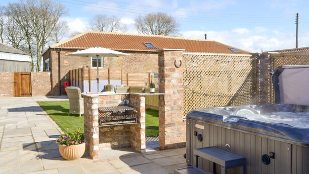 Un'area patio con una vasca idromassaggio, un barbecue e un angolo salotto con tavolo e sedie.