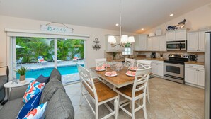 A spacious kitchen with white cabinets, a wooden dining table, and a view of a swimming pool.