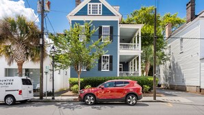 A two-story house with a balcony, a red car parked in front, and a white van with "COUNTER CULTURE COFFEE" on the side. - Easy Walk to King Street! | Casa Fuego Suite E (Charleston)