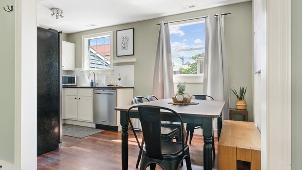 A kitchen with white cabinets, a microwave, and a dishwasher. There is a dining table with chairs and a window with curtains. - Easy Walk to King Street! | Casa Fuego Suite E (Charleston)
