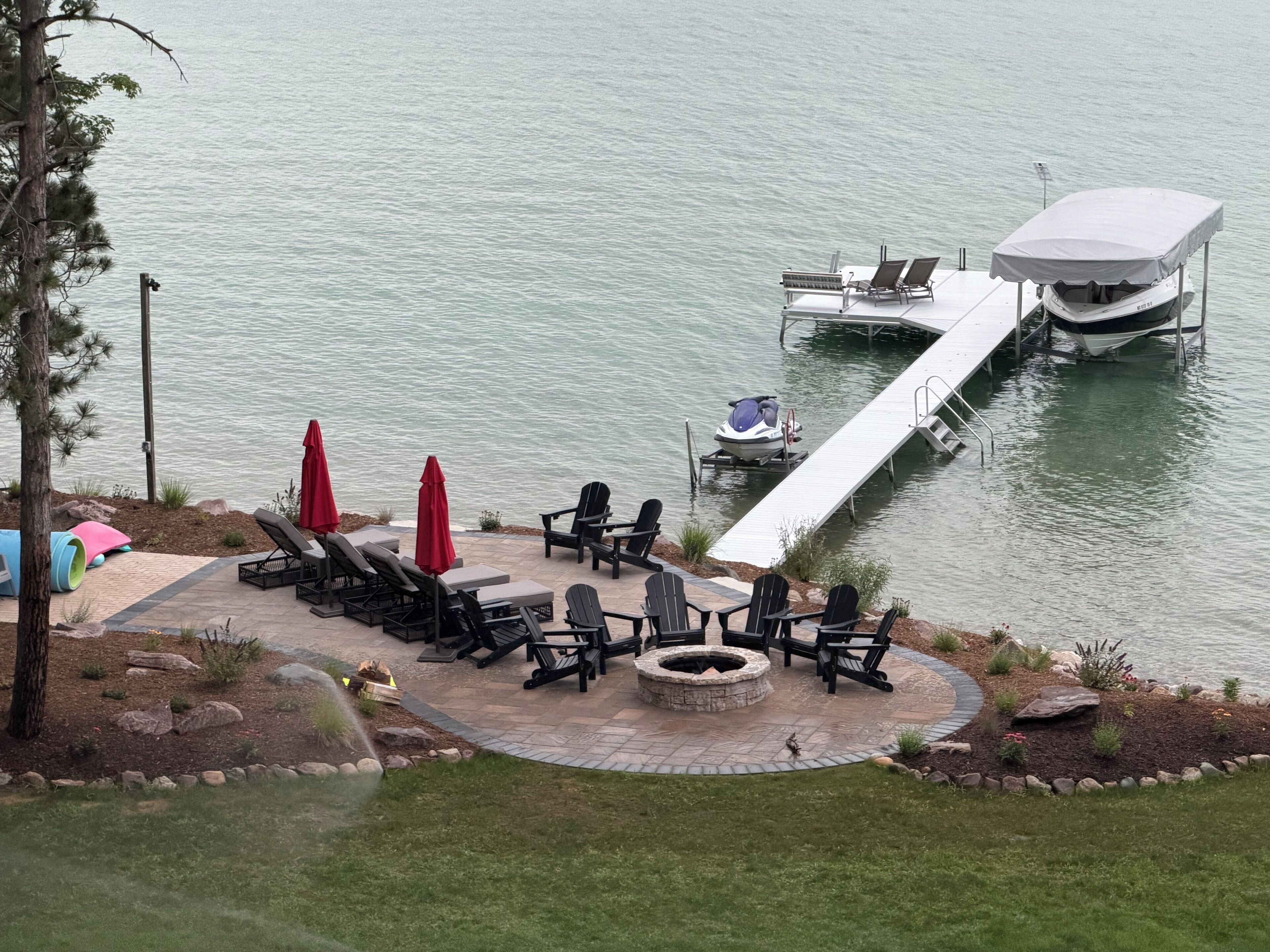 A lakeside patio with lounge chairs, a fire pit, and a jet ski dock.