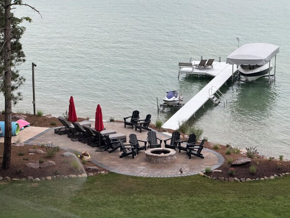 A lakeside patio with lounge chairs, a fire pit, and a jet ski dock.