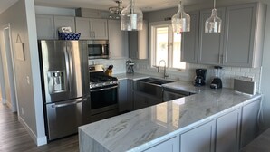 A modern kitchen with stainless steel appliances, a marble countertop, and pendant lighting.