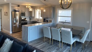 A modern kitchen with a central island, stainless steel appliances, pendant lighting, and a dining area with a bench.