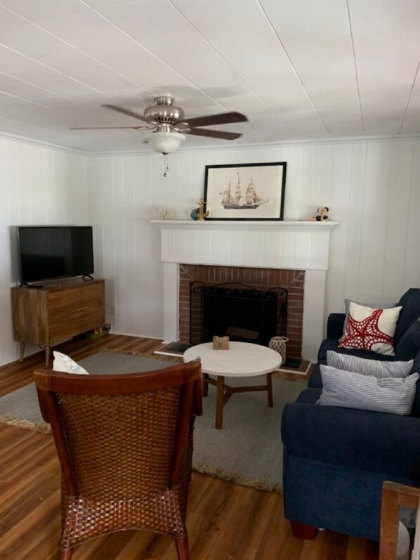 Una sala de estar con chimenea, televisor, ventilador de techo y sofá.