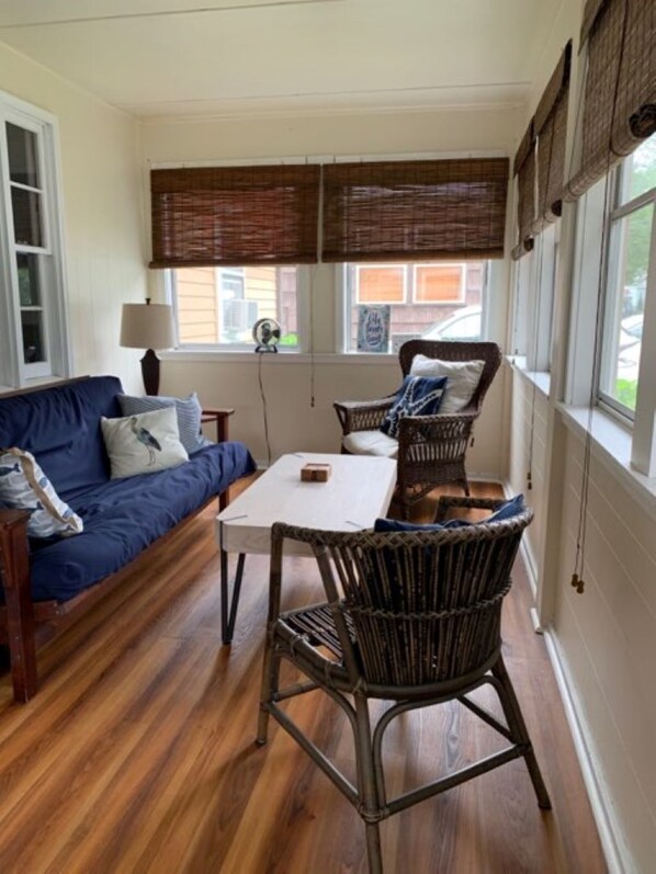 A cozy room with a blue sofa, wicker chairs, a small table, and large windows with blinds.