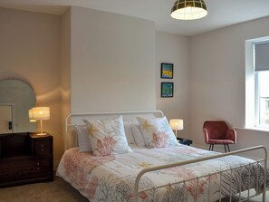 A bedroom with a bed, bedside lamps, a dresser, a chair, and two wall-mounted pictures.