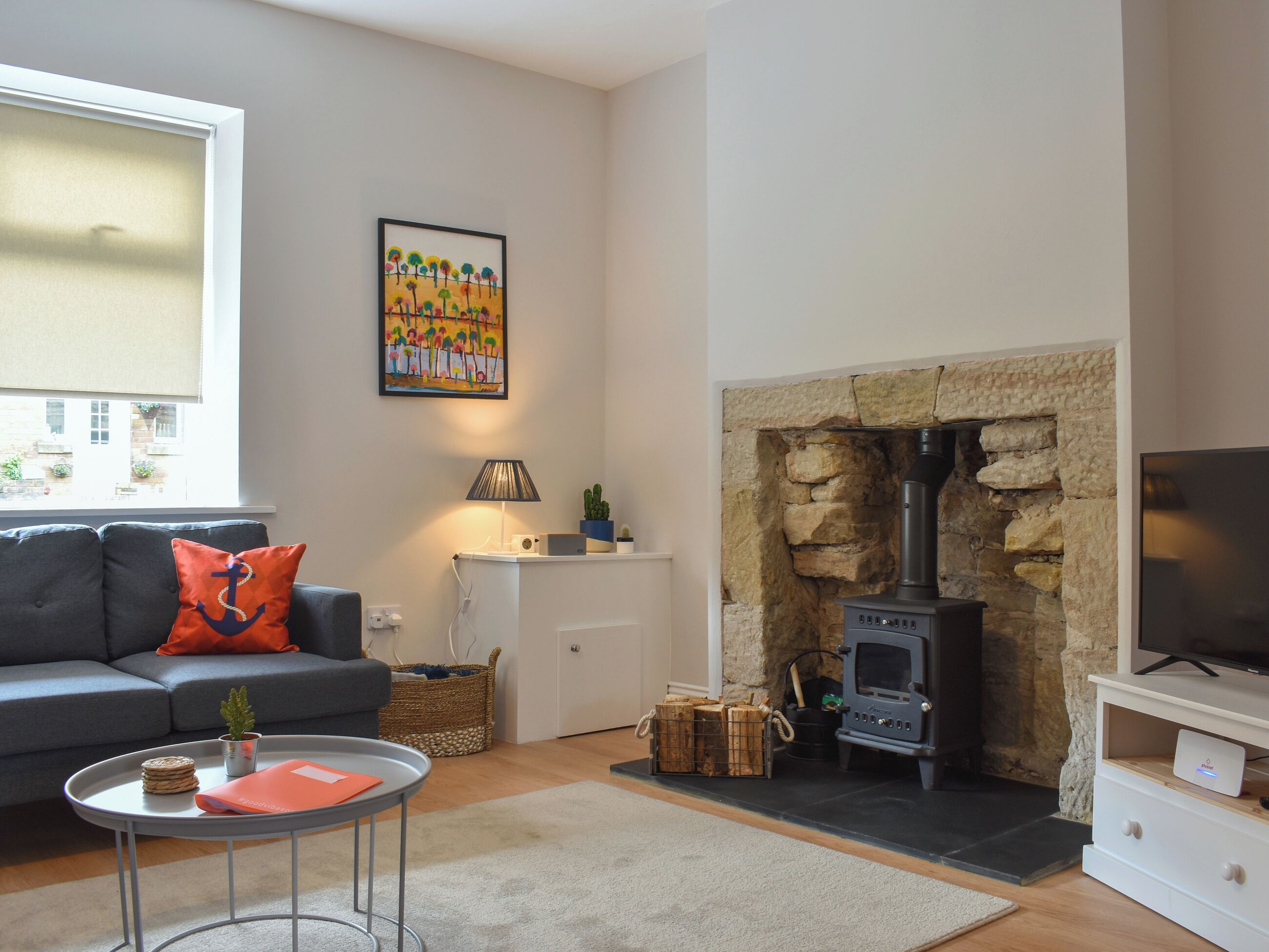 A living room with a sofa, a table with a plant, a fireplace with a stone wall, and a TV on a stand.