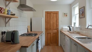 A kitchen with a wooden countertop, a gas stove, a white refrigerator, and a wooden door. - 3 bedroom accommodation in Amble, near Morpeth (Amble, near Morpeth)
