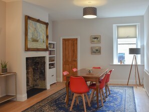 A dining room with a fireplace, a table with chairs, a bookshelf, and a window with a view.