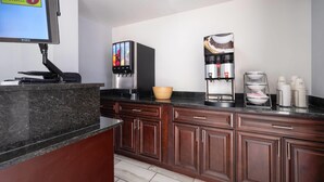 A modern kitchen with a coffee station, a large screen, and a bowl on the counter. - Super 8 by Wyndham Portsmouth - Norfolk (Portsmouth)