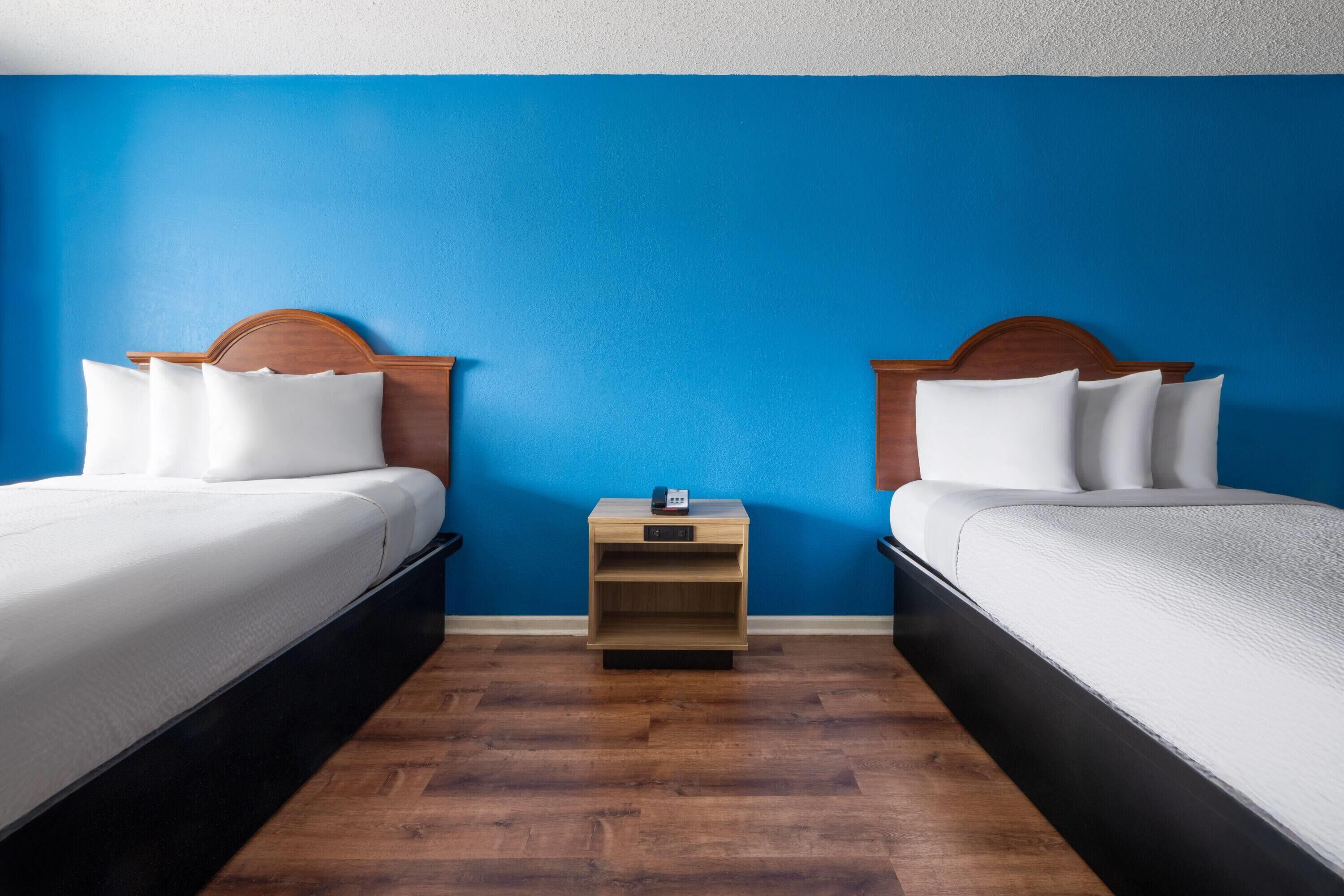 A hotel room with two beds, a nightstand, and a blue wall.