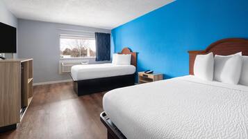 A hotel room with two beds, a TV, a window with curtains, and a wooden wardrobe.