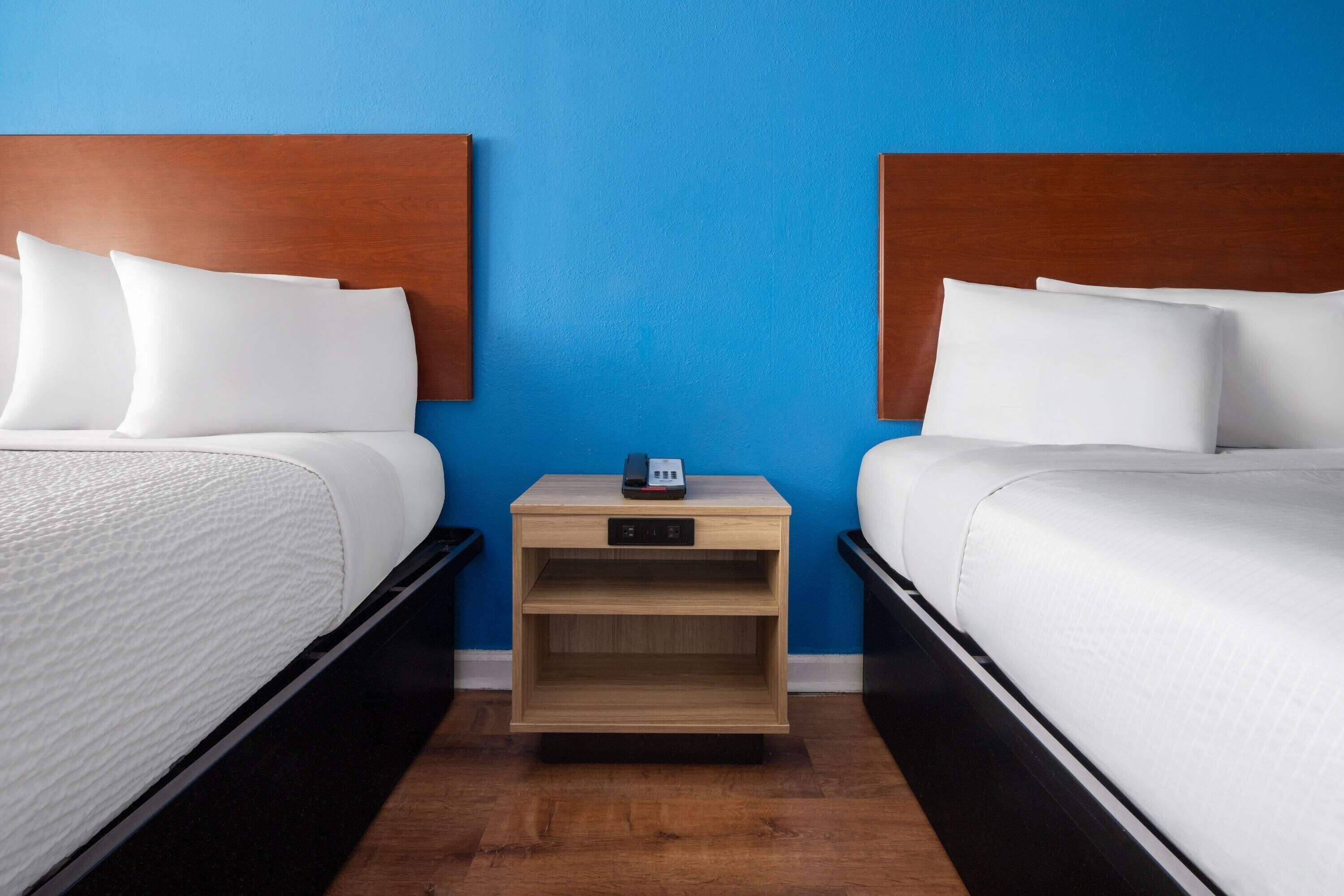 A hotel room with two beds, a nightstand, and a blue wall.