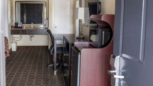 A compact hotel room with a kitchenette, a large mirror, a door, and a patterned floor. - Oregon Trail Inn and Suites (Lakeview)