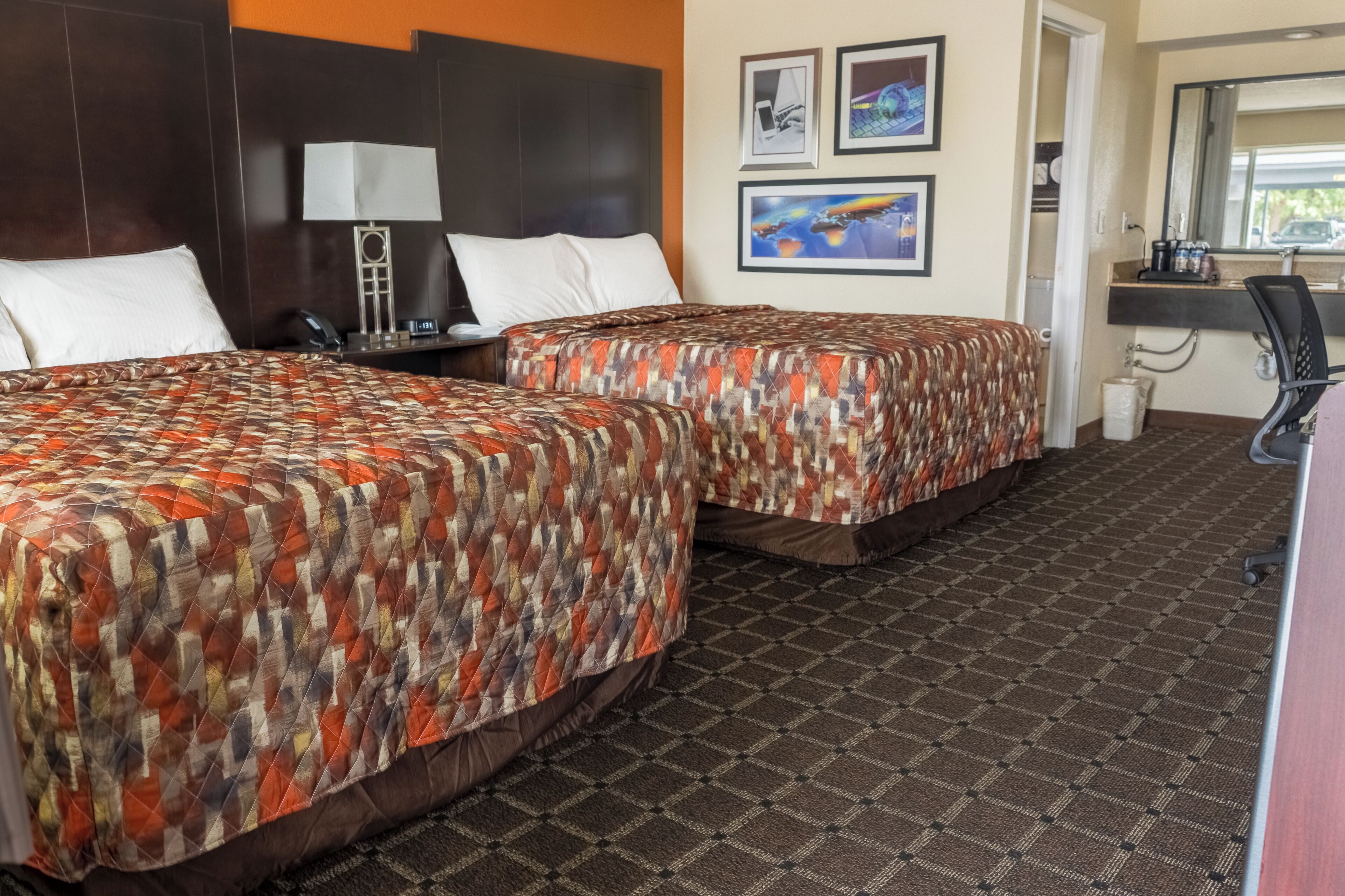 Une chambre d’hôtel avec deux lits, un bureau, une chaise, une lampe et des œuvres d’art accrochées au mur.