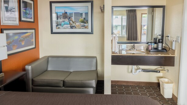 A hotel room with a sofa, a cityscape picture, a sink, and a mirror. - Oregon Trail Inn and Suites (Lakeview)