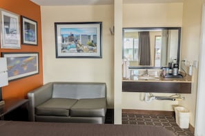 A hotel room with a sofa, a cityscape picture, a sink, and a mirror.