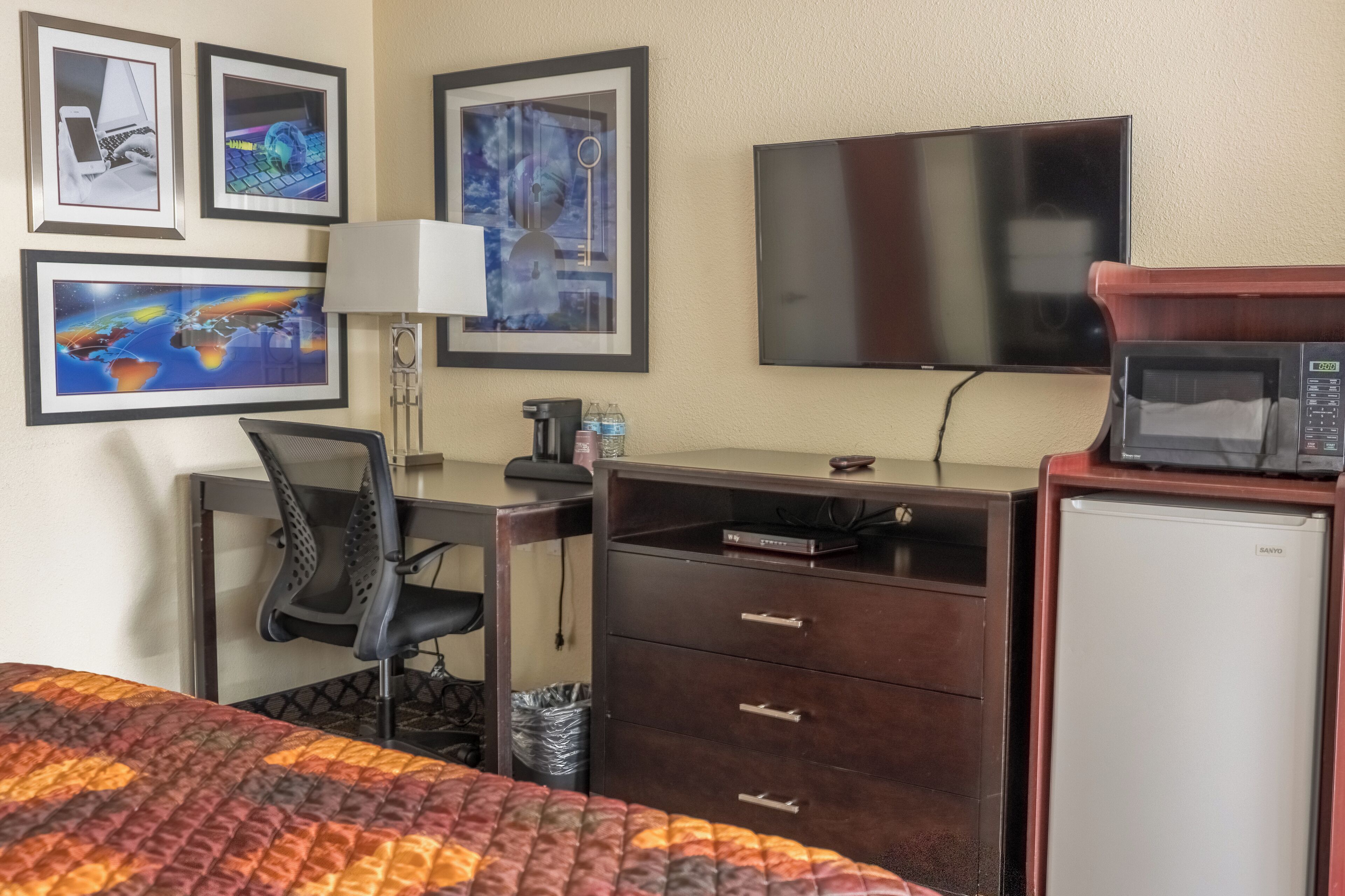 A hotel room with a bed, desk, chair, television, microwave, and a small refrigerator.