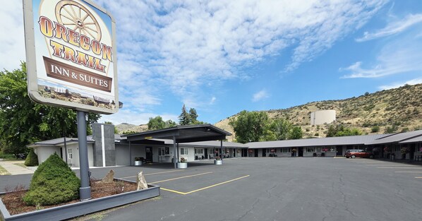 A motel with a large sign, covered parking, and a mountainous backdrop.