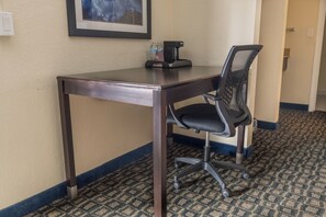 A hotel room with a dark wooden desk, a black office chair, a framed picture on the wall, and a patterned carpet. - Oregon Trail Inn and Suites (Lakeview)