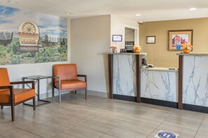A hotel reception area with a marble counter, a sign for Oregon Trail Inn & Suites, and a seating area with leather chairs. - Oregon Trail Inn and Suites (Lakeview)
