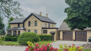 Ein großzügiges, zweistöckiges Haus mit Ziegelaußenwand, einer Garage und einem gepflegten Rasen mit blühenden Pflanzen.